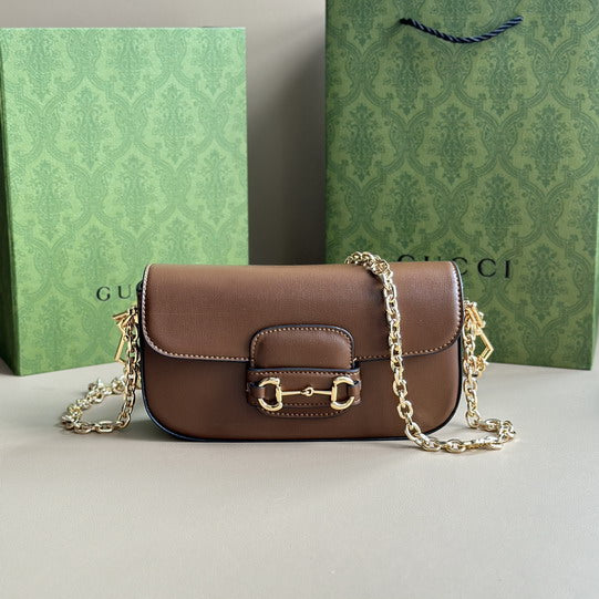 Gucci Horsebit 1955 Mini Bag in brown leather with gold chain strap, displayed with Gucci green gift boxes