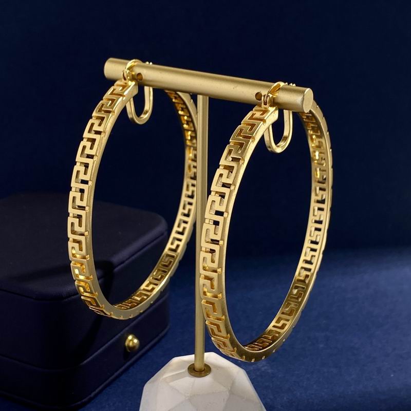 Gold Greek key pattern hoop earrings displayed on a jewelry stand against a dark blue background